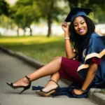 Excellence Scholarship female-graduate-student-wearing-a-mortarboard-sitting-on-a-curb-in-a-park