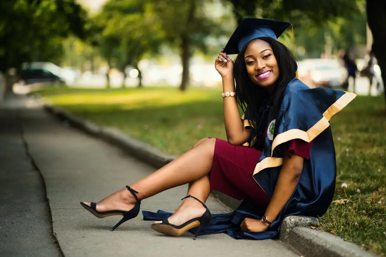 Excellence Scholarship female-graduate-student-wearing-a-mortarboard-sitting-on-a-curb-in-a-park