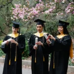 utrecht excellence scholarship students-in-graduation-gowns-and-hats-unfolding-certificates-and-magnolia-in-background