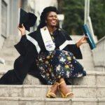 a fellowship award-woman-wearing-academic-dress-and-floral-dress-sitting-on-stairway